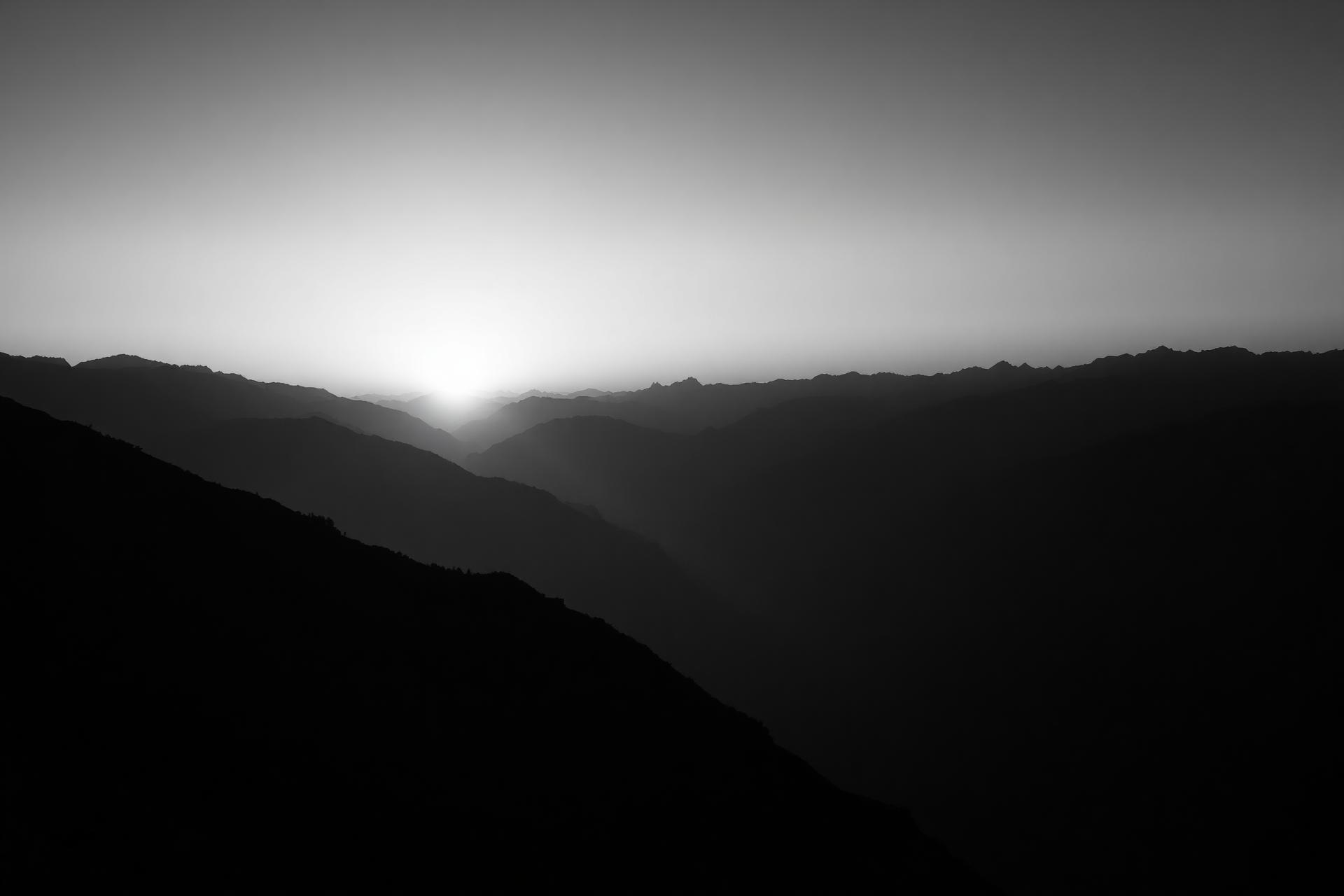 Black and white mountain skyline at dawn, layered ridges fading into mist.